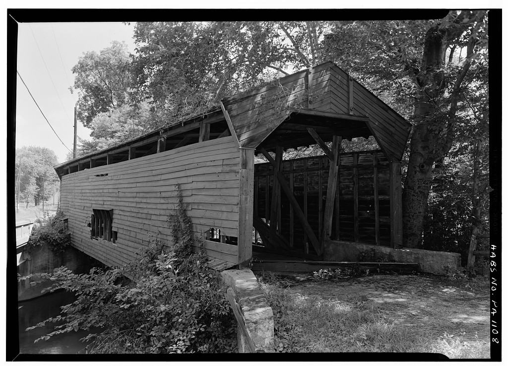 a black and white photo shows a covered bridge in need of repair