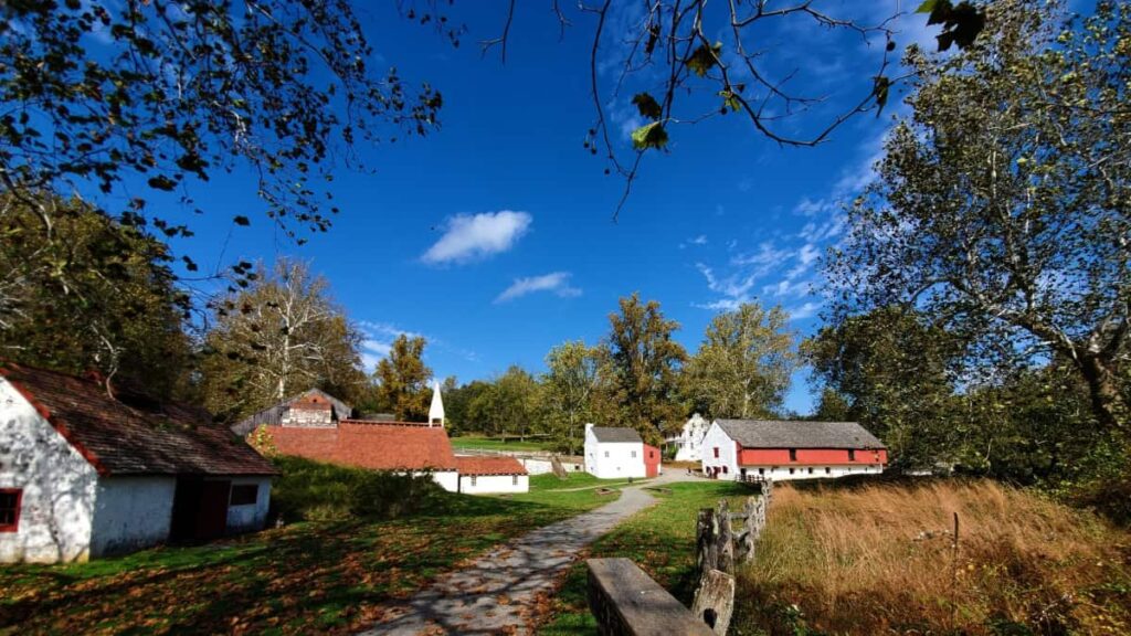 White buildings with red roofs are seen in the distance while visiting Hopewell Furnace in French Creek State Park