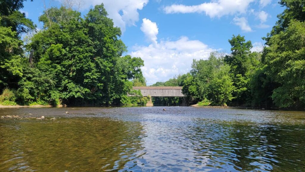 Looking towards a grey covered bridge while sitting in the Neshaminy Creek at Tyler State Park