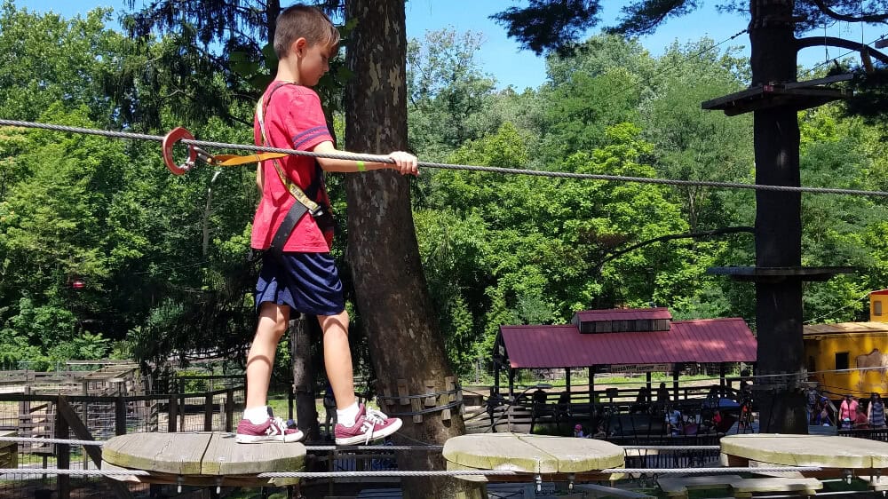 A young boy walks across a ropes course obstacle