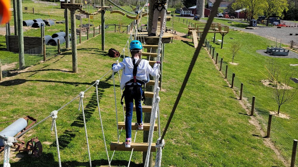 A young girl crosses a rope obstacle at Hellericks Farm