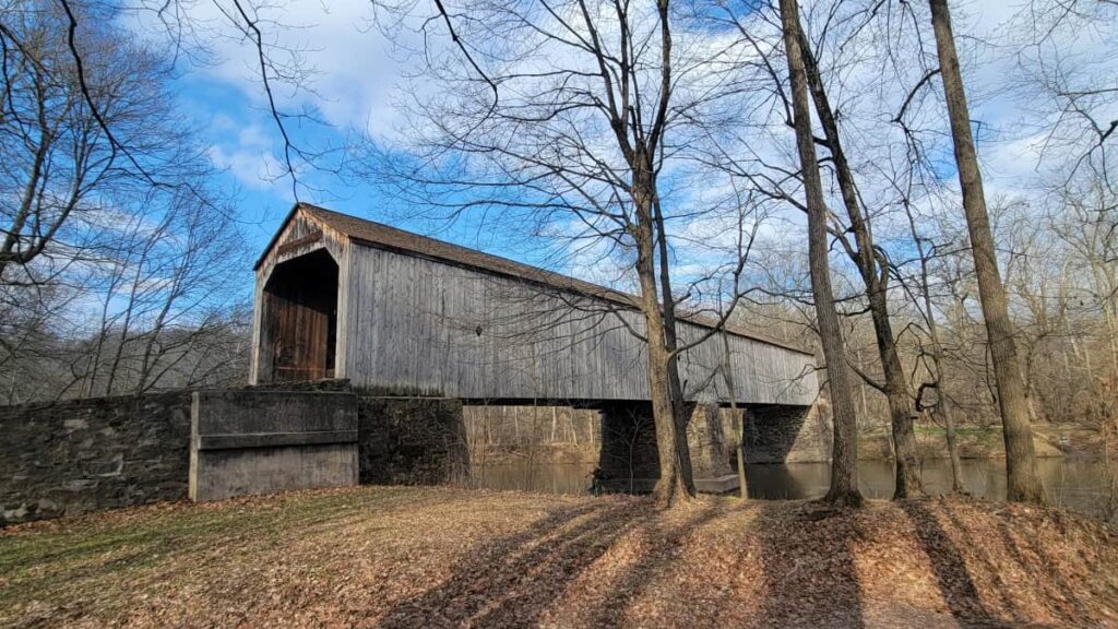 A gray wooden covered bridge in Tyler State Park spans the Neshaminy creek in the late fall