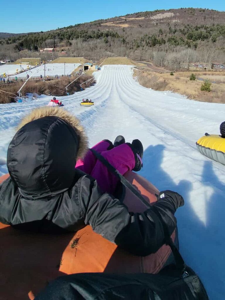 A girls wearing a black coat sits on a snow tube at the top of a hill