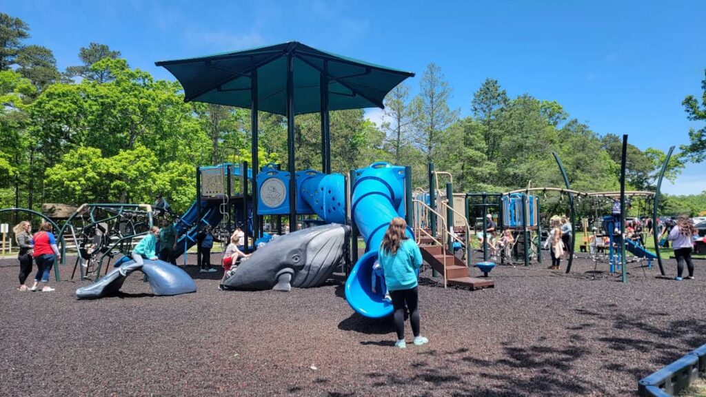 A blue plaground structure has several kids and parents on and nearby