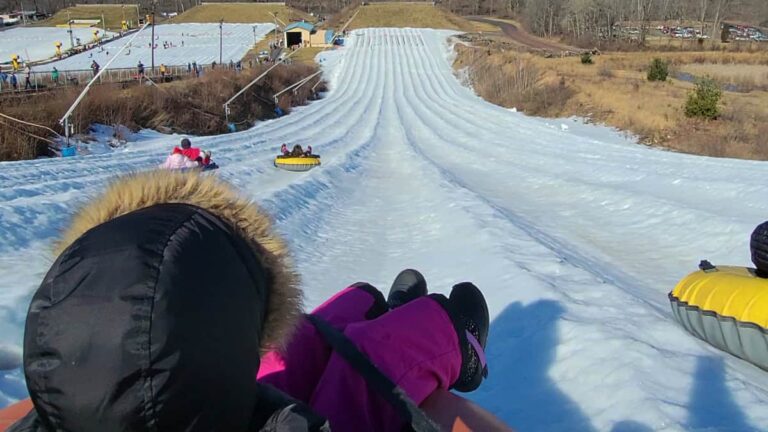 A girls wearing a black coat sits on a snow tube at the top of a hill