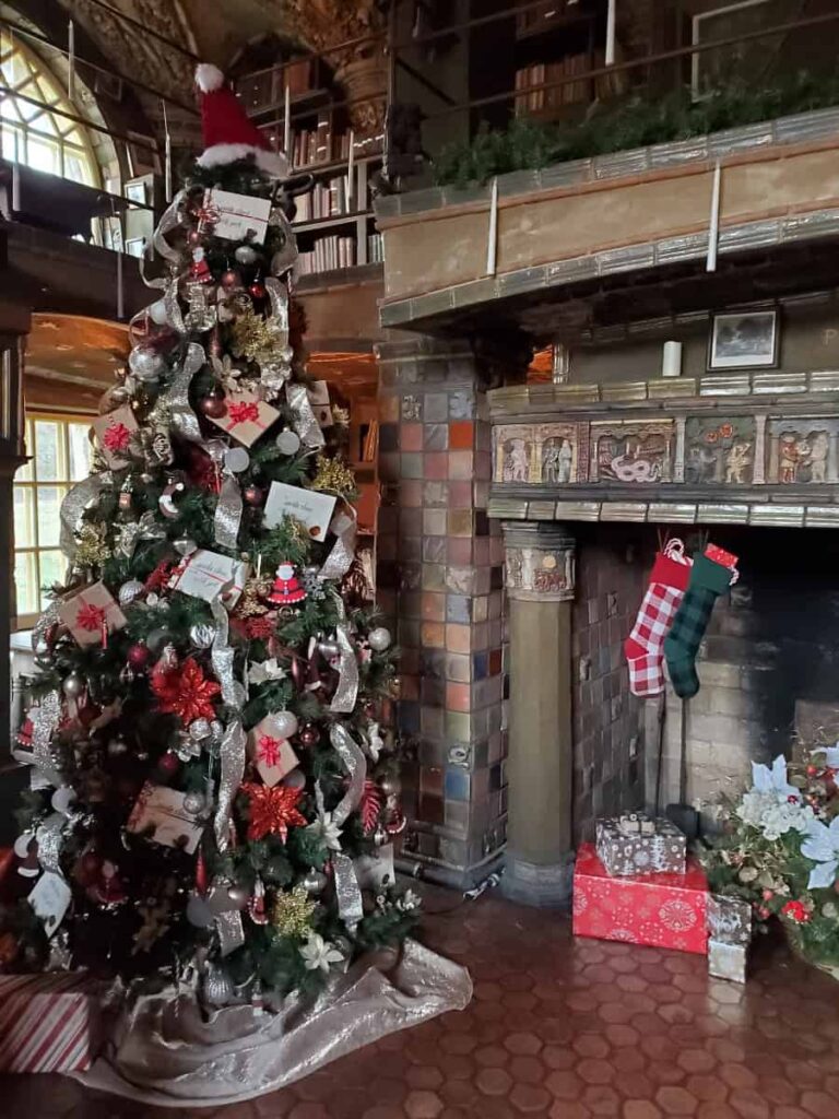 A decorated tree sits tot he left of a fireplace inside the library at Fonthill Castle