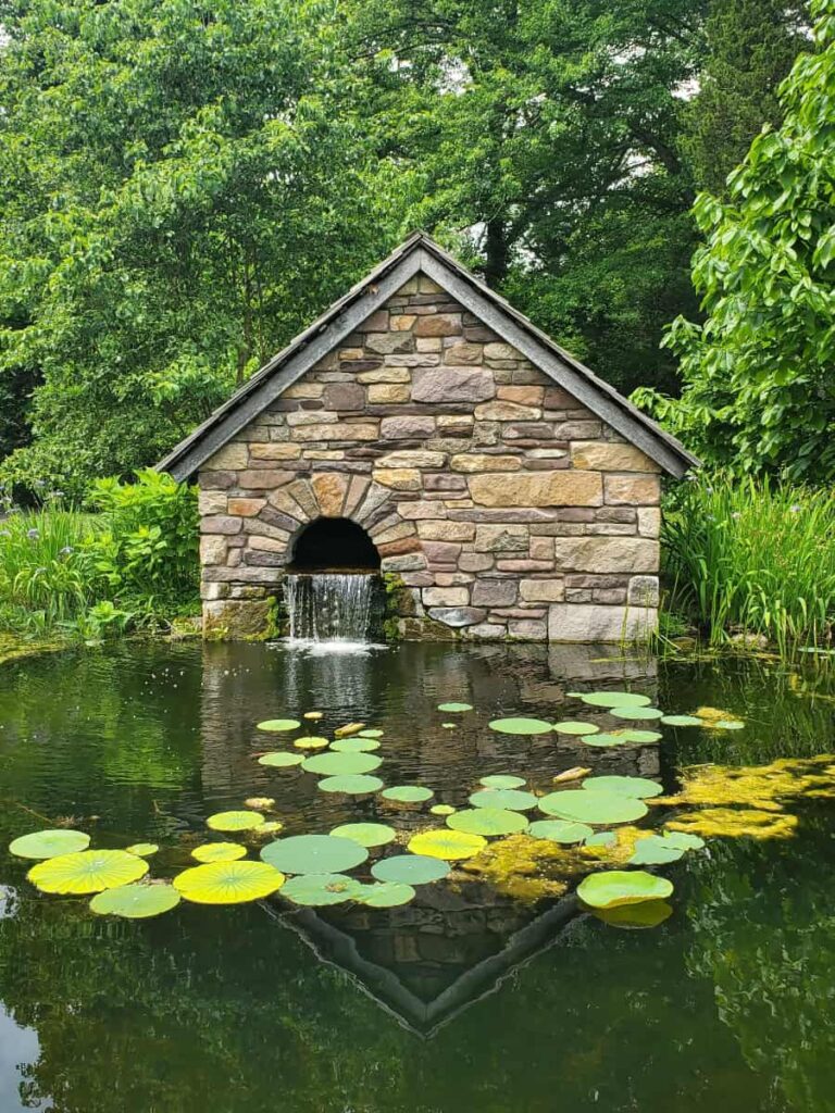 A stone triangular shaped building sits at the edge of a small pond