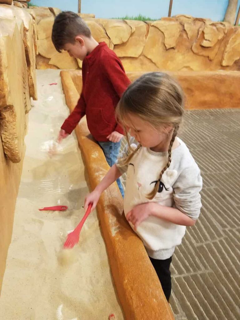 Two kids dig through sand looking for "dinosaur" bones at the Bucks County Children's Museum