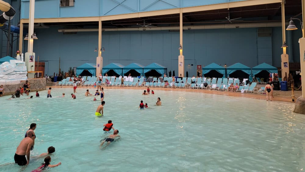 People swim in an indoor wavepool with chairs at the water's edge