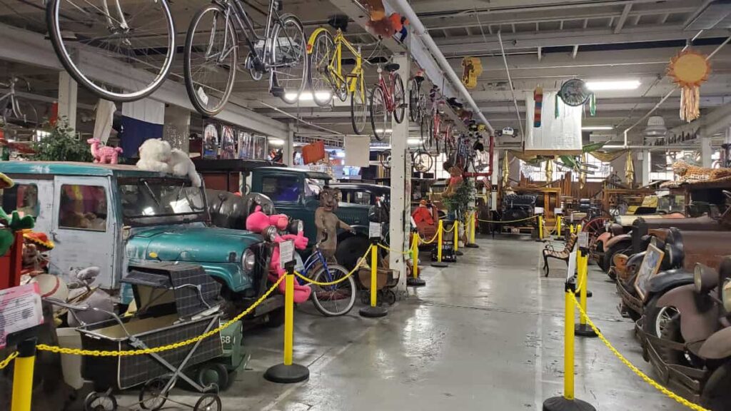 Classic cars are lined up facing each other with bicycles hanging overhead at the American Treasure Tour Museum