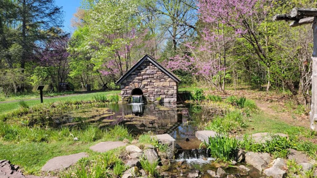 a stone pump house sits at the edge of a small pond in early spring